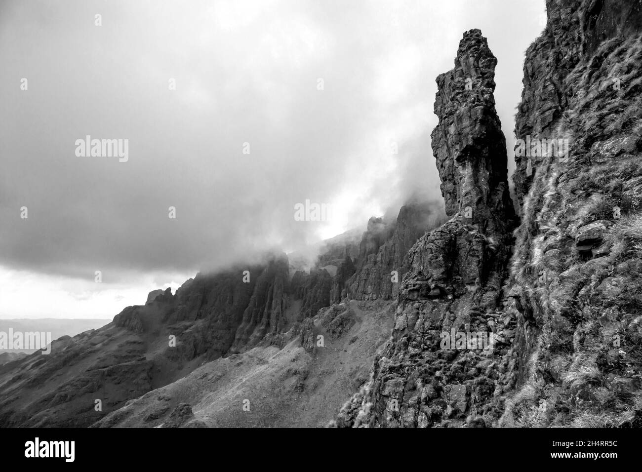 Eine verwitterte Basaltsäule, mit Nebel, der im Hintergrund die Klippen herabkommt, in den Drakensberg Mountains an der Grenze zwischen Südafrika und Leso Stockfoto