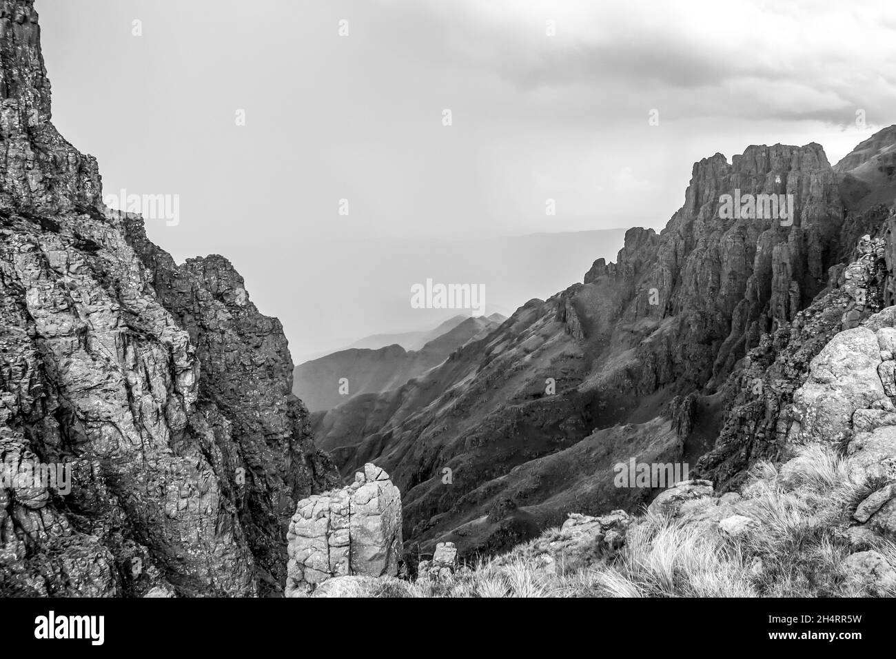 Schwarz-Weiß Blick entlang der zackigen, verwitterten Basaltklippen des Organ Passes in den Drakensberg Bergen von Südafrika, mit Regen im Hintergrund Stockfoto