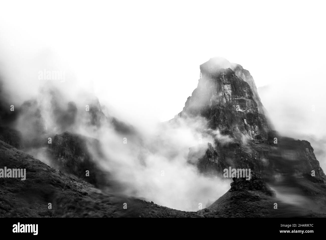 Die hohen Basaltgipfel der Drakensberg Mountains in Südafrika, teilweise verdeckt durch dichten Nebel, der sich um sie herum sammelt. Diese steilen Klippen und Gipfel w Stockfoto