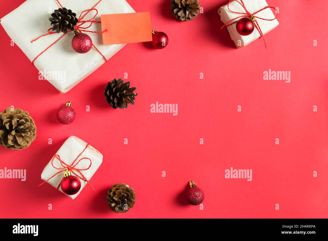 Die Neujahrsgeschenke sind in Bastelpapier gewickelt und mit einem roten Gummis gebunden, liegen zwischen den Kugeln und Zapfen auf einem roten Hintergrund. Handgefertigte Verpackung. Draufsicht. Stockfoto
