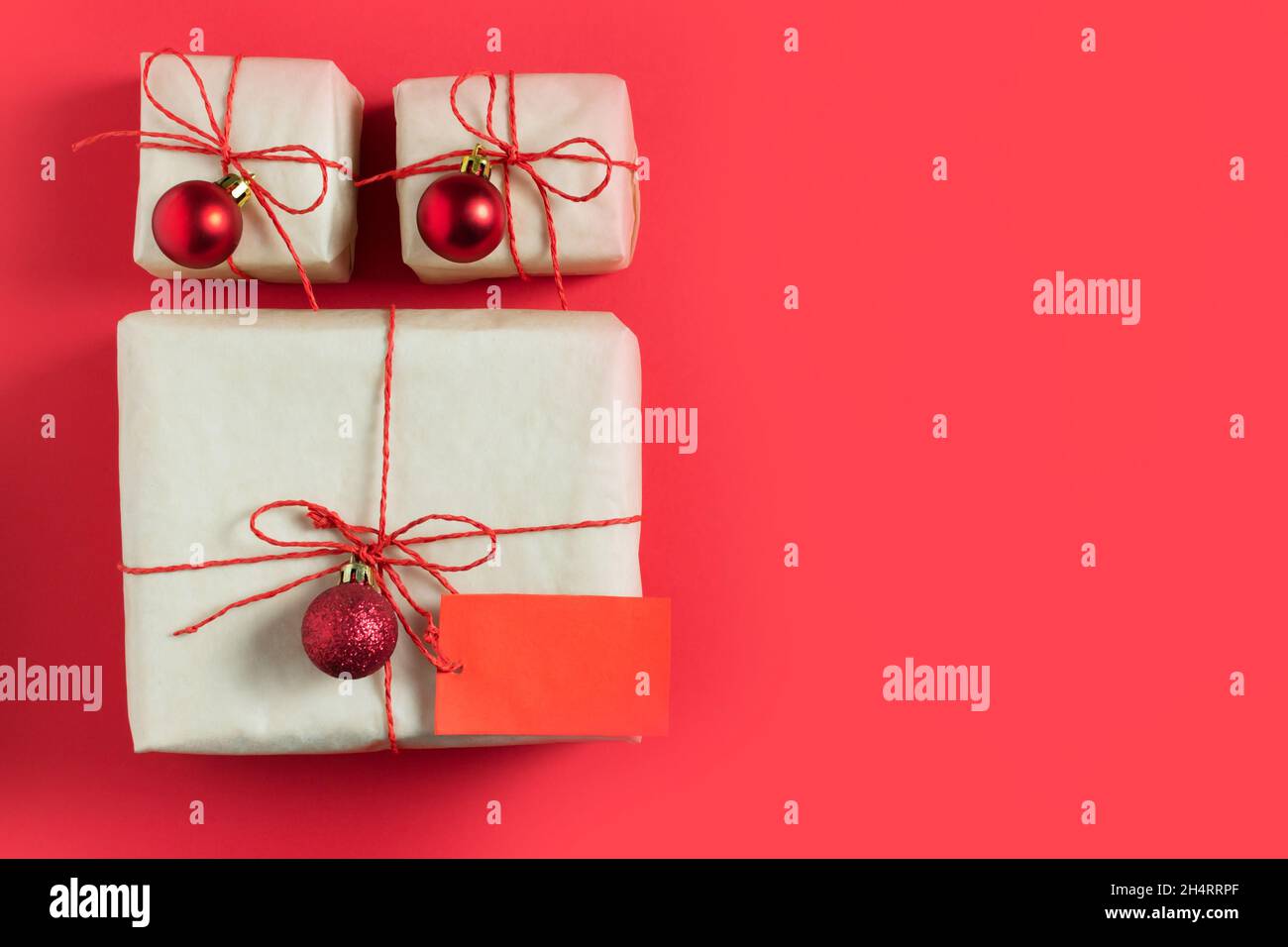 Die Neujahrsgeschenke sind in Bastelpapier gewickelt und mit rotem Jgut und kleinen Weihnachtskugeln auf rotem Hintergrund gebunden. Handgefertigte Verpackung. Draufsicht. Kopie en Stockfoto