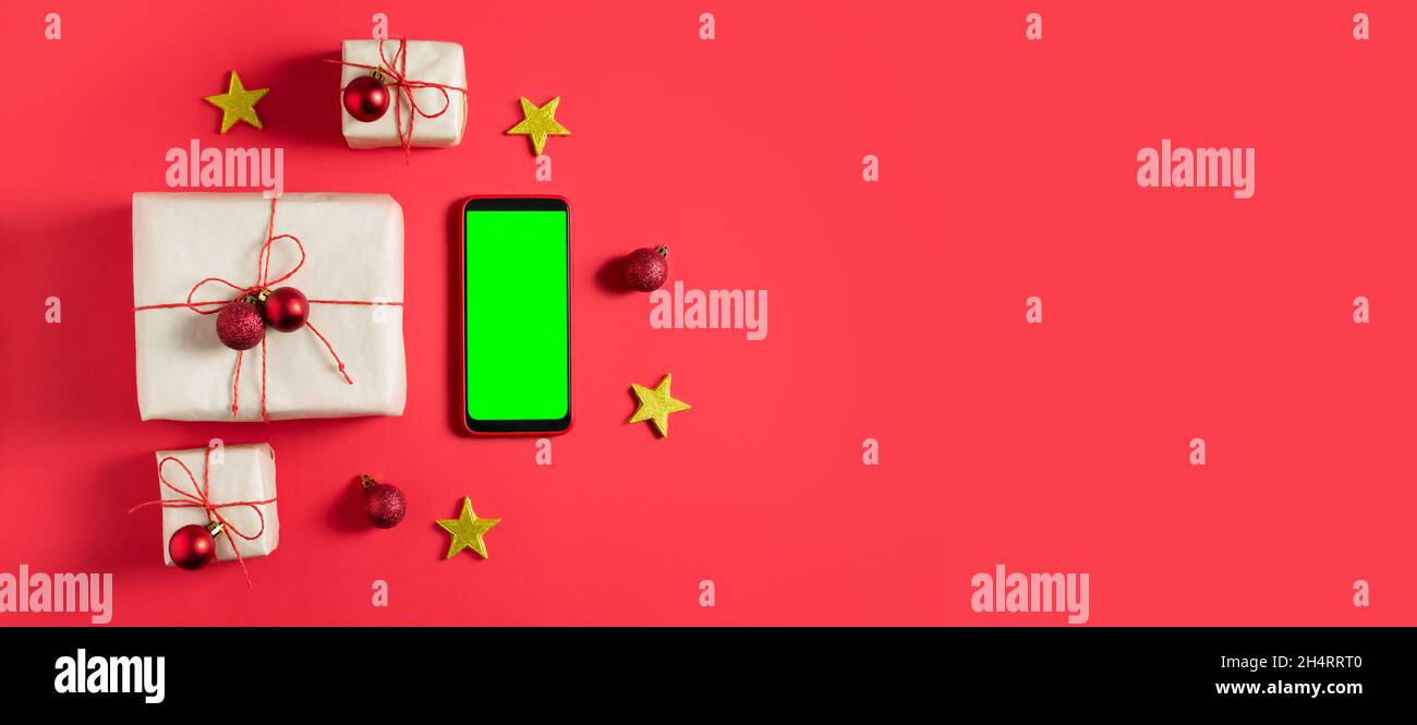 Die Neujahrsgeschenke sind in Bastelpapier verpackt und mit rotem Jgut und kleinen Weihnachtskugeln auf rotem Hintergrund gebunden. Grünes Handy-Display, Chroma-Taste Stockfoto