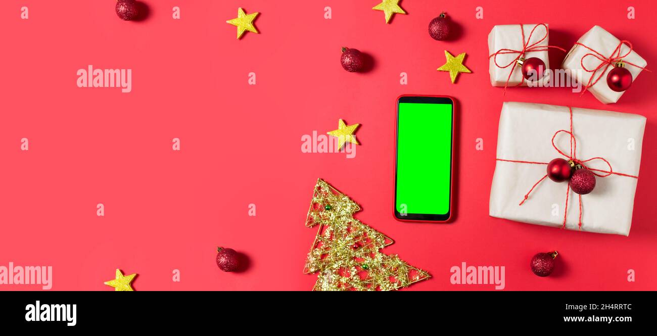 Die Neujahrsgeschenke sind in Bastelpapier verpackt und mit rotem Jgut und kleinen Weihnachtskugeln auf rotem Hintergrund gebunden. Grünes Handy-Display, Chroma-Taste Stockfoto
