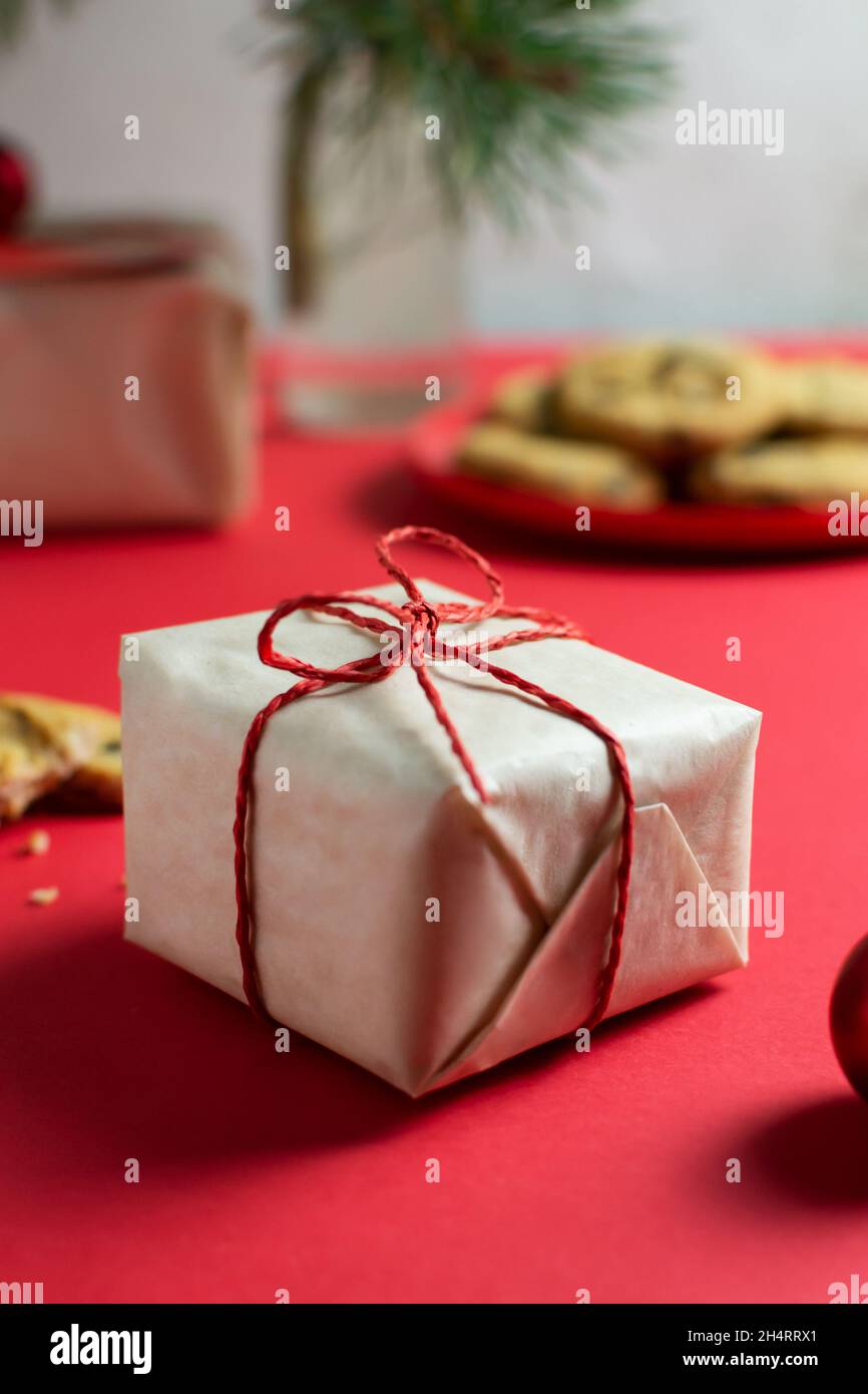 Ein kleines Neujahrsgeschenk ist in Bastelpapier, einem Teller mit Keksen und einem Glas Milch auf dem Tisch, einer Vase mit Tannenzweigen verpackt. Selektiver Fokus. Ch Stockfoto