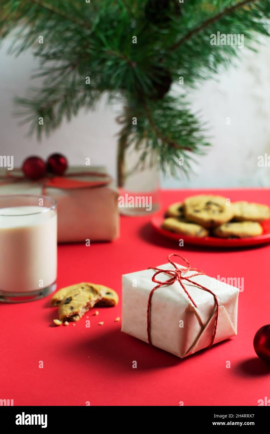 Ein kleines Neujahrsgeschenk ist in Bastelpapier, einem Teller mit Keksen und einem Glas Milch auf dem Tisch, einer Vase mit Tannenzweigen verpackt. Selektiver Fokus. Ch Stockfoto