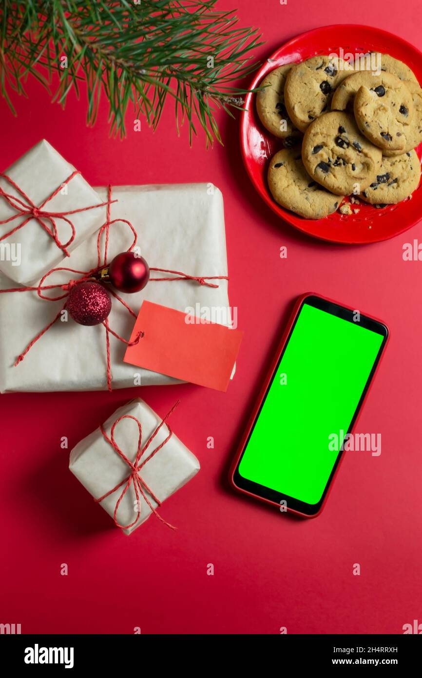 Die Neujahrsgeschenke sind in Bastelpapier verpackt, einem Plätzchen mit Schokolade auf rotem Hintergrund. Grünes Handy-Display, Chroma-Taste. Online-Geschenk Stockfoto