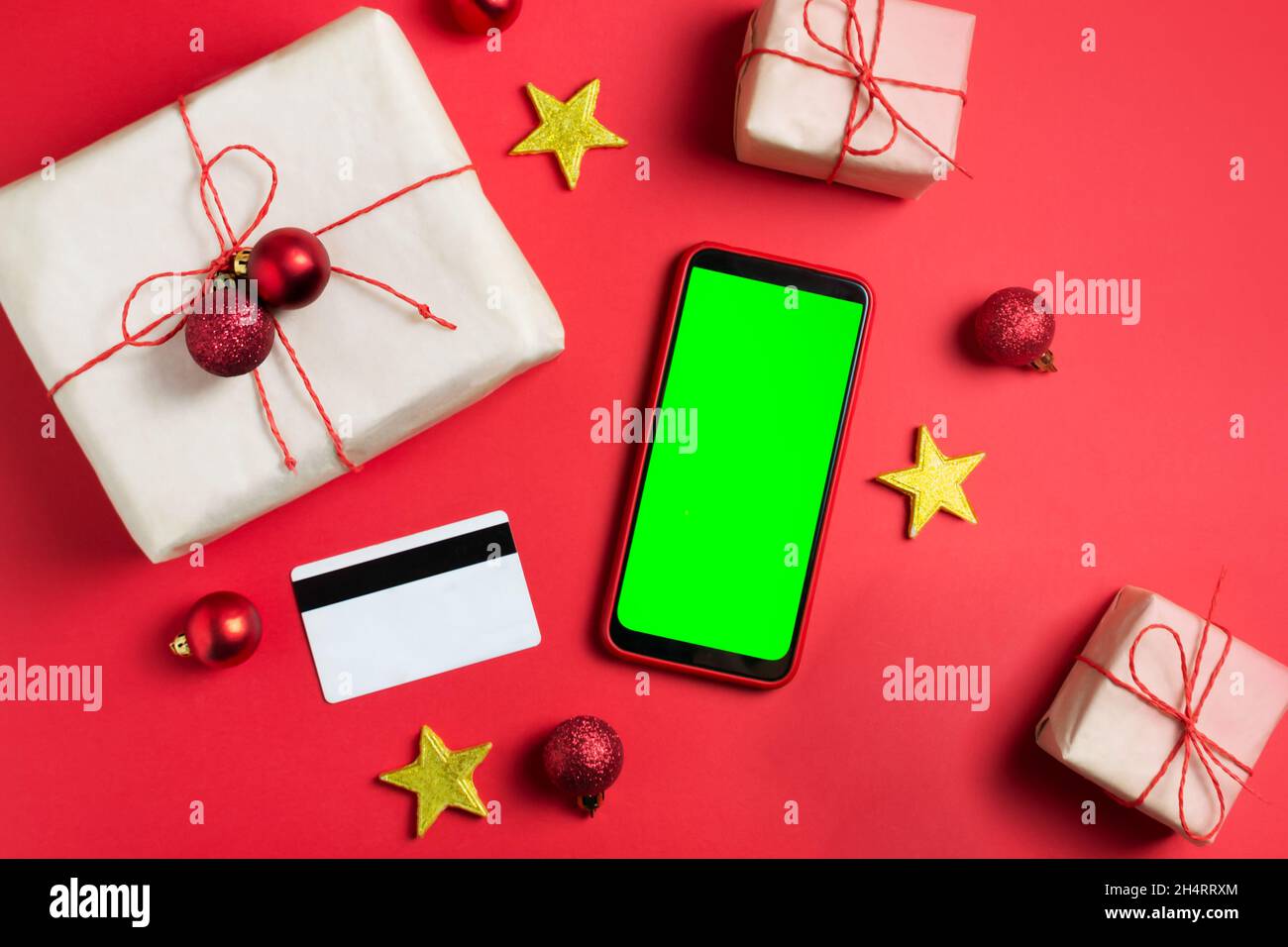 Die Neujahrsgeschenke sind in Bastelpapier, einem Mobiltelefon mit grünem Bildschirm, einem Chroma-Schlüssel und einer Kreditkarte auf rotem Hintergrund verpackt. Online-Geschenkshoppi Stockfoto