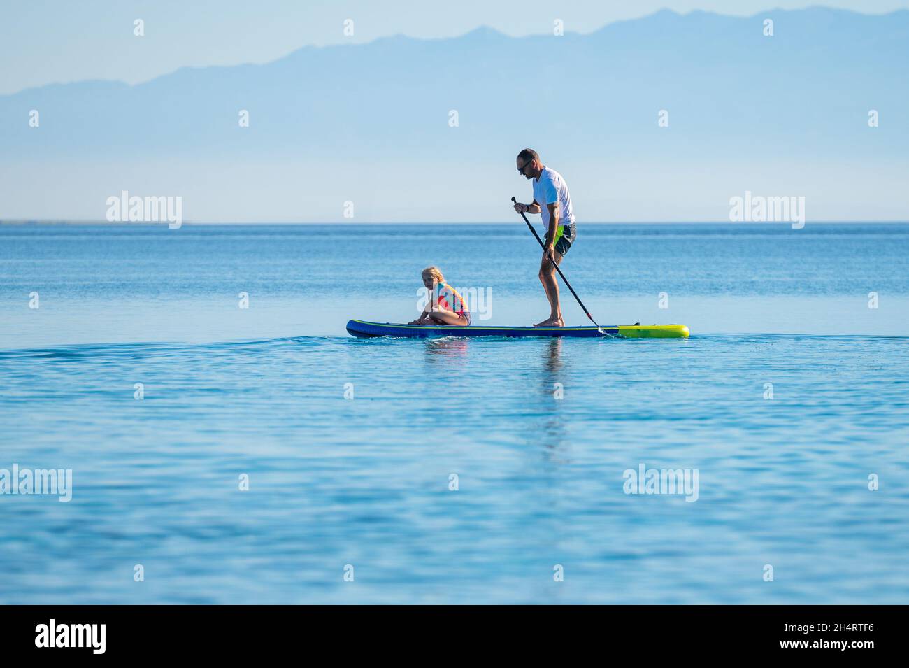 Vater und Tochter reiten auf SUP Stand Up Paddle im Urlaub. Aktive Familie, die SUP-Boards reitet und am schönen Abend im Meer paddelt. Athlet Stockfoto