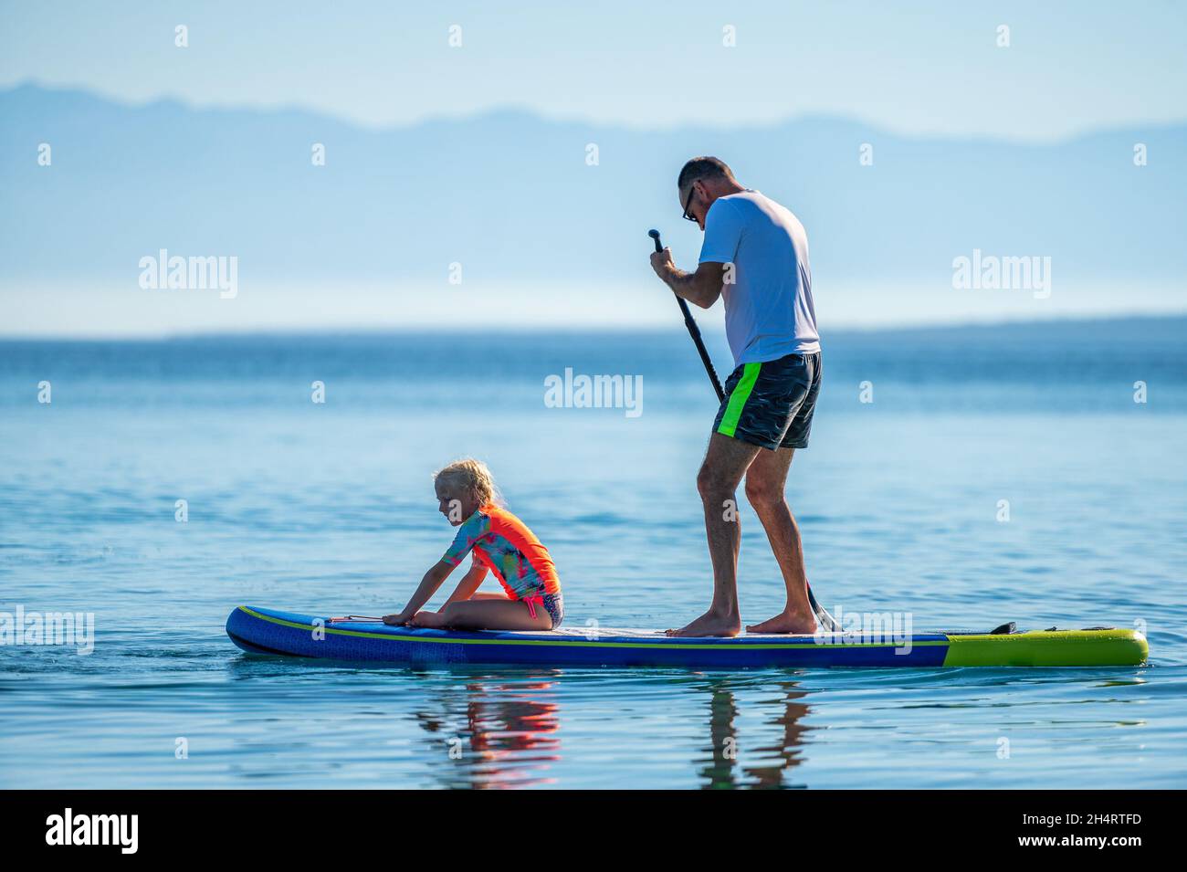 Vater und Tochter reiten auf SUP Stand Up Paddle im Urlaub. Aktive Familie, die SUP-Boards reitet und am schönen Abend im Meer paddelt. Athlet Stockfoto