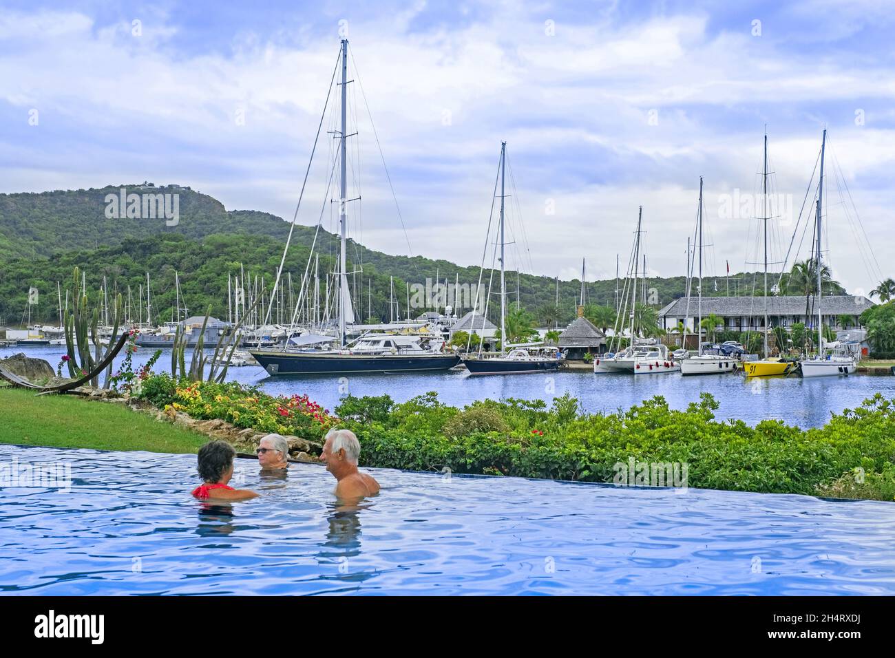 Segelboote und Yachten liegen im englischen Hafen und westliche Touristen im Schwimmbad auf der Insel Antigua, kleine Antillen in der Karibik Stockfoto