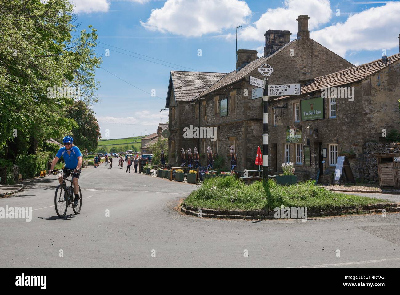 Radfahren in Yorkshire, Blick im Sommer auf einen Mann, der am historischen Buck Inn im Zentrum des malerischen Dorfs Yorkshire Dales in Malham, England, vorbeiradelt Stockfoto