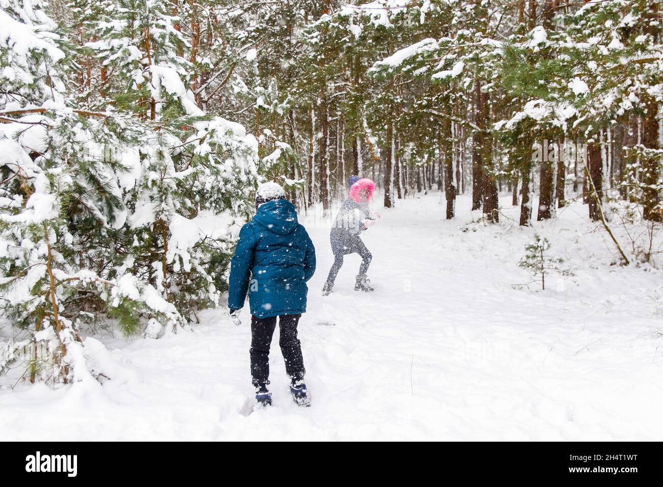 Der Junge wirft einen Schneeball auf das Mädchen. Lustige Kinder im Winter Park spielen Schneebälle und verbringen aktiv Zeit im Freien. Winter verschneiten Wald. Kalt f Stockfoto