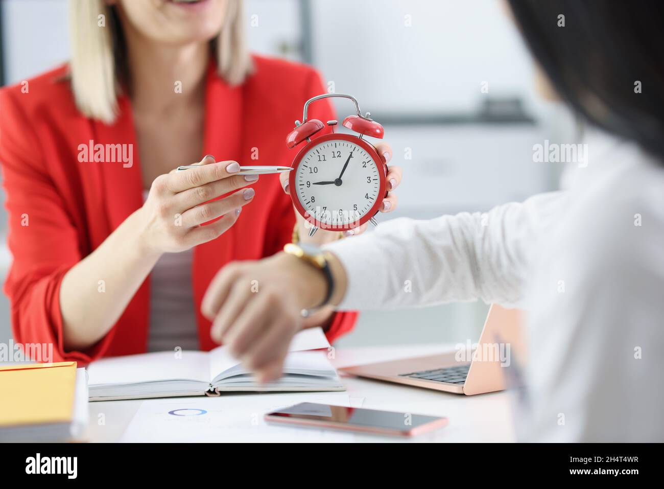 Nahaufnahme der Chefin beschimpft den Mitarbeiter, weil er spät zur Arbeit kommt, und zeigt mit dem Stift auf die rote Uhr. Rüge von Geschäftsfrau zu Arbeiterin, Reminde Stockfoto