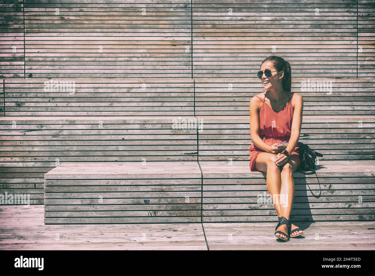 New York City Lifestyle junge Frau sitzt auf High Line Park Bank in NYC. Tourist Asian Mädchen mit Handy genießen Sommer Reise Urlaub Stockfoto