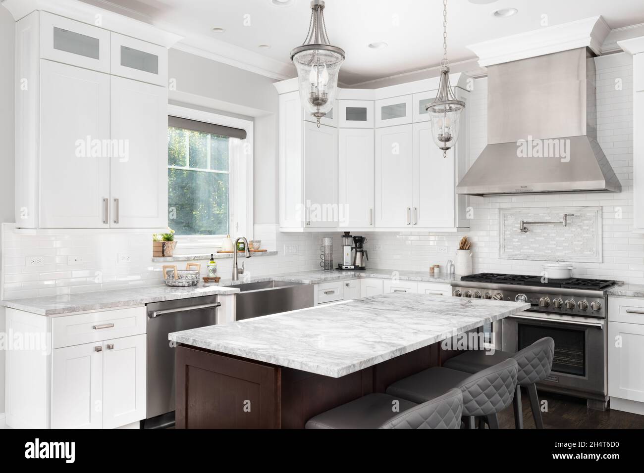 Eine luxuriöse weiße Küche mit einer großen Insel, Edelstahlgeräten und U-Bahnfliesen-Backsplash. Stockfoto