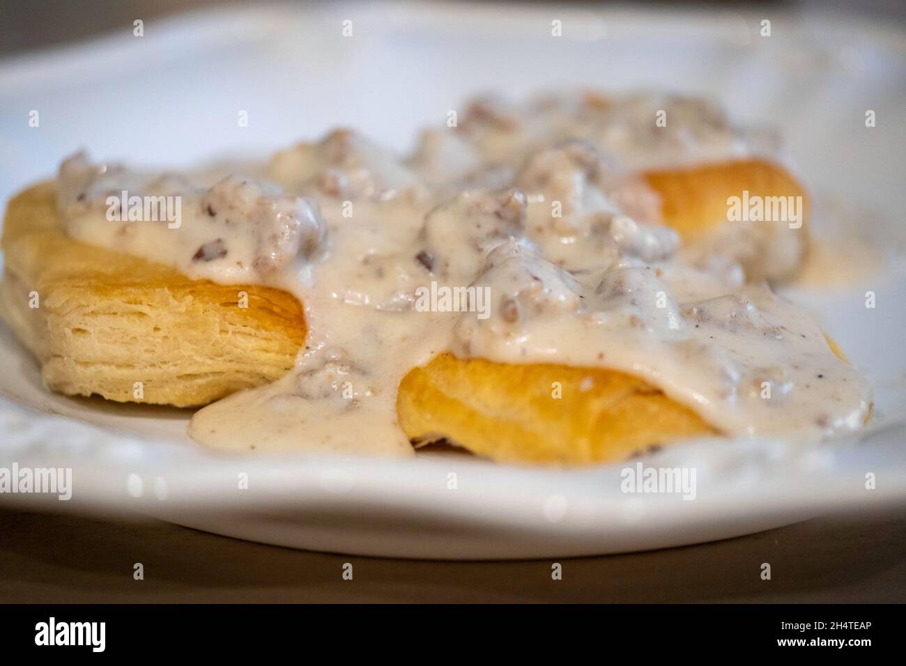 Auf einem weißen Teller mit einer gewürfelten Milchgravie mit Schweinewurst über Keksen. Stockfoto