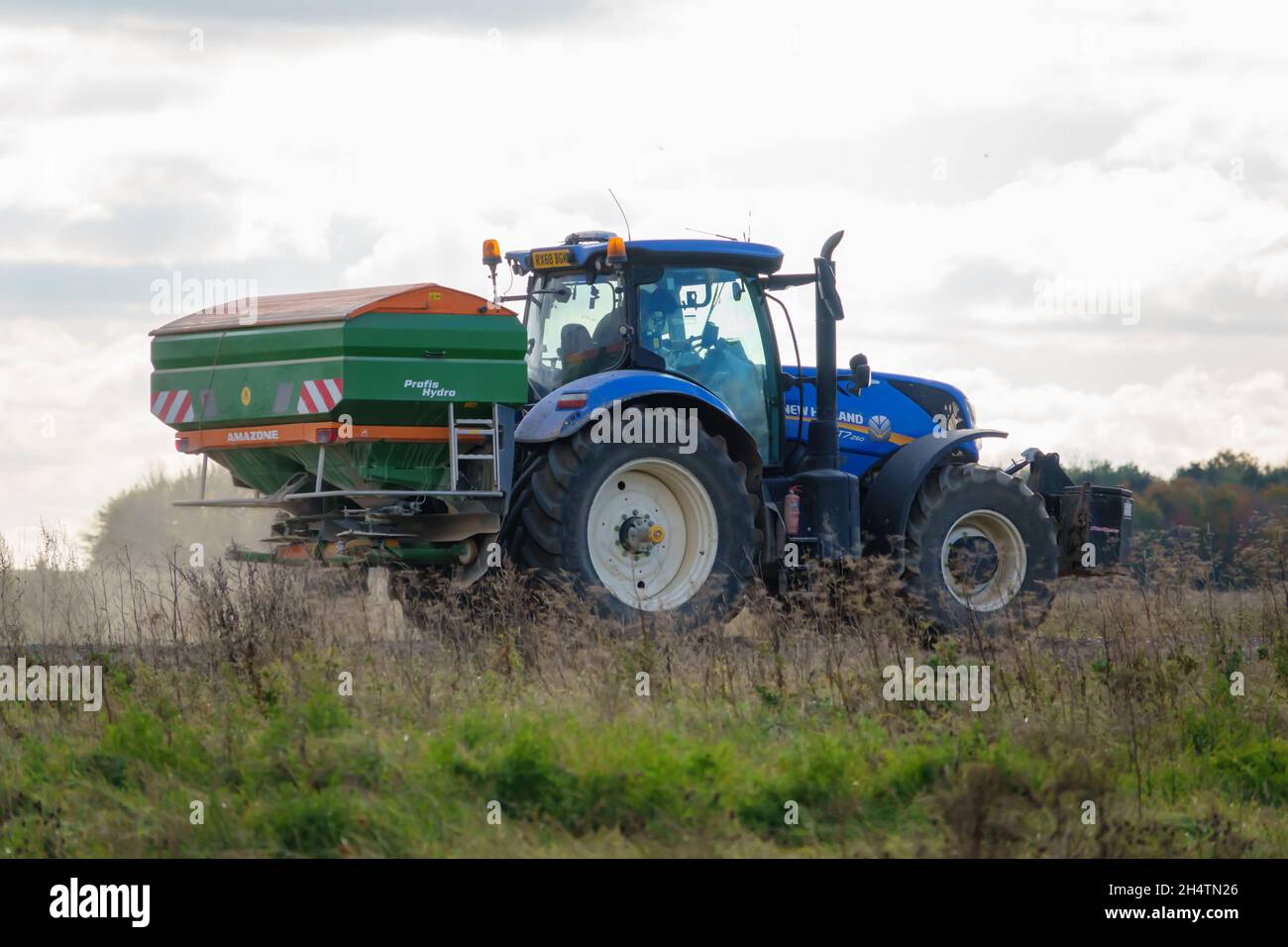 Großer blauer New Holland T7 225 Traktor in Aktion mit montiertem Amazone Profis Hydra ZA-TS Spreader Stockfoto