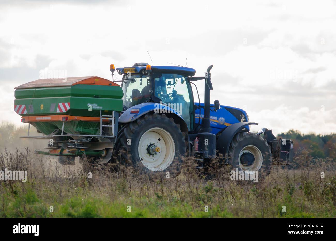 Großer blauer New Holland T7 225 Traktor in Aktion mit montiertem Amazone Profis Hydra ZA-TS Spreader Stockfoto