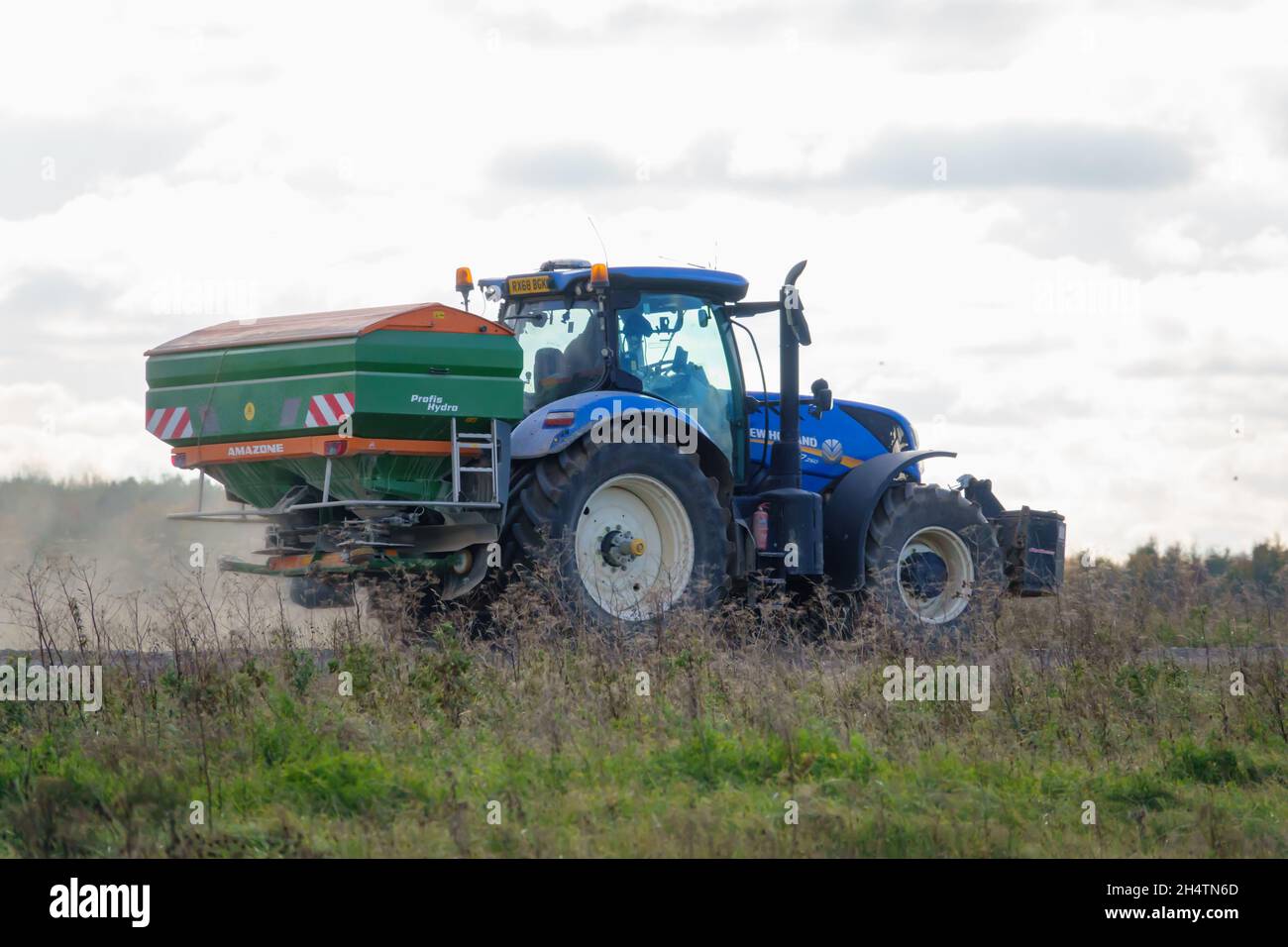 Großer blauer New Holland T7 225 Traktor in Aktion mit montiertem Amazone Profis Hydra ZA-TS Spreader Stockfoto