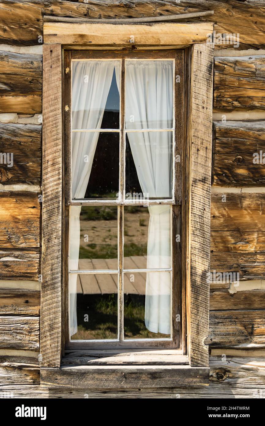Altes verwittertes Holzfenster mit Vorhang in rustikaler Blockhütte Stockfoto