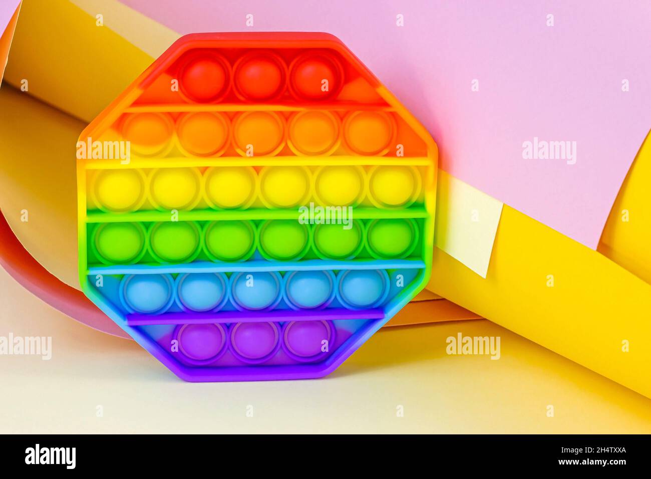 Trendy einfache Grübchen oder Pop it Sinnesspielzeug für Kinder auf hellem Papier Hintergrund. Beliebte Antistress Silikon Kinder Blase Fidget in Regenbogenfarben. Stockfoto