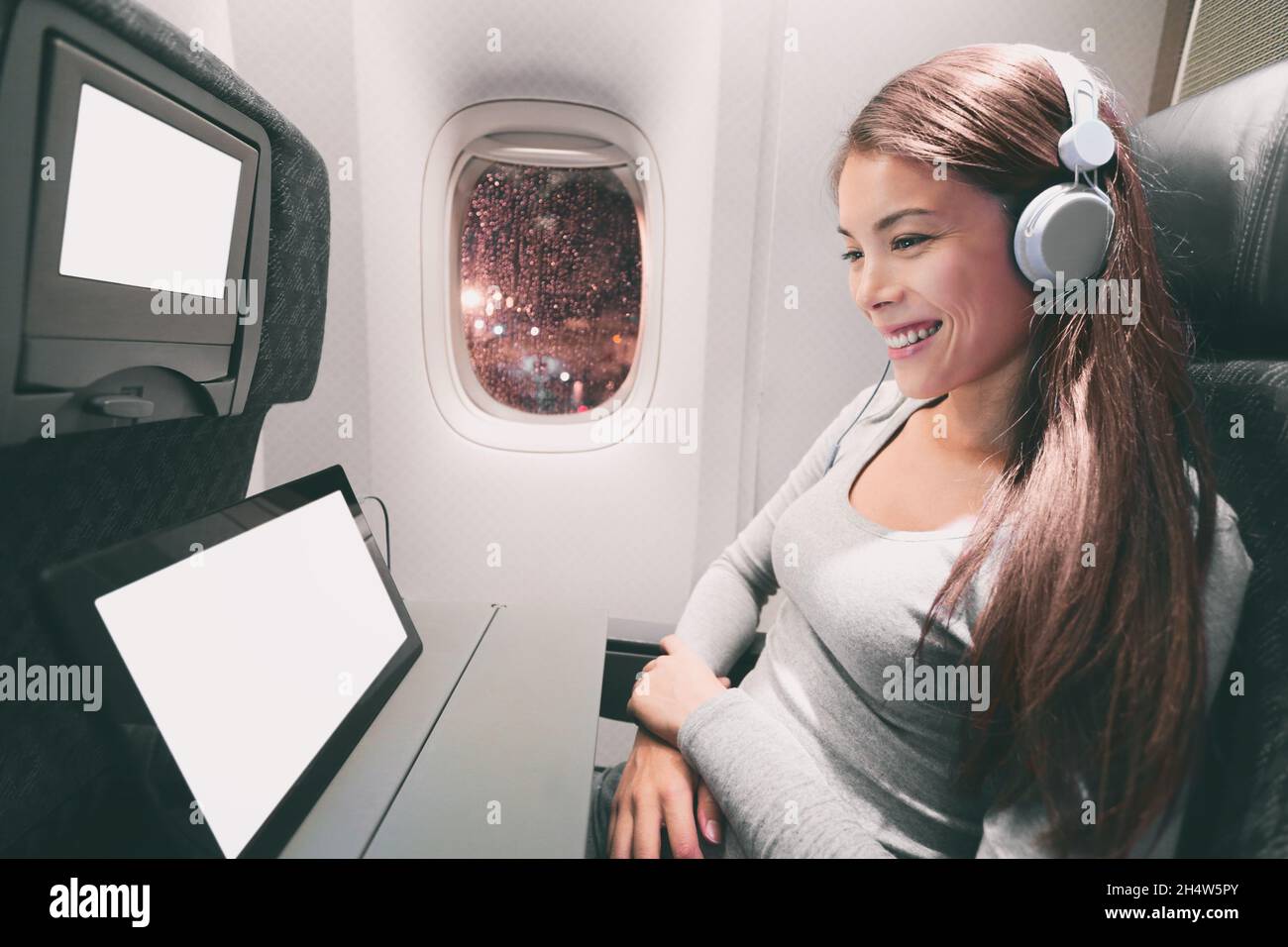 Passagier im Flugzeug mit Tablet-Computer. Frau in der Flugzeugkabine mit einem intelligenten Gerät, das Musik über Kopfhörer hört. Banner Panorama Reisen Menschen Stockfoto