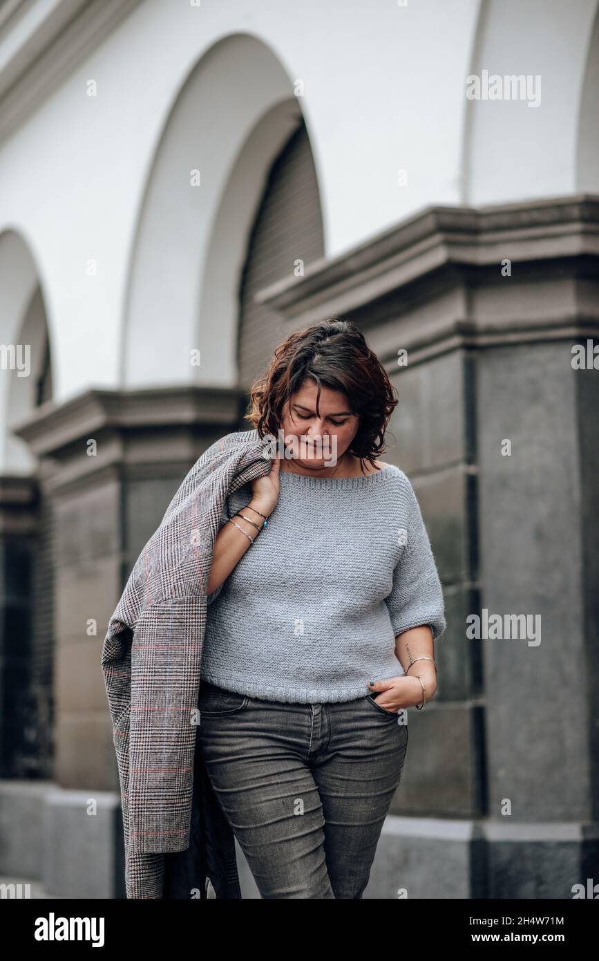 Ein Tourist schaut nach unten, während er seine lange Jacke auf dem Hintergrund der antiken Architektur an der Schulter hält. Vertikales Bild Stockfoto