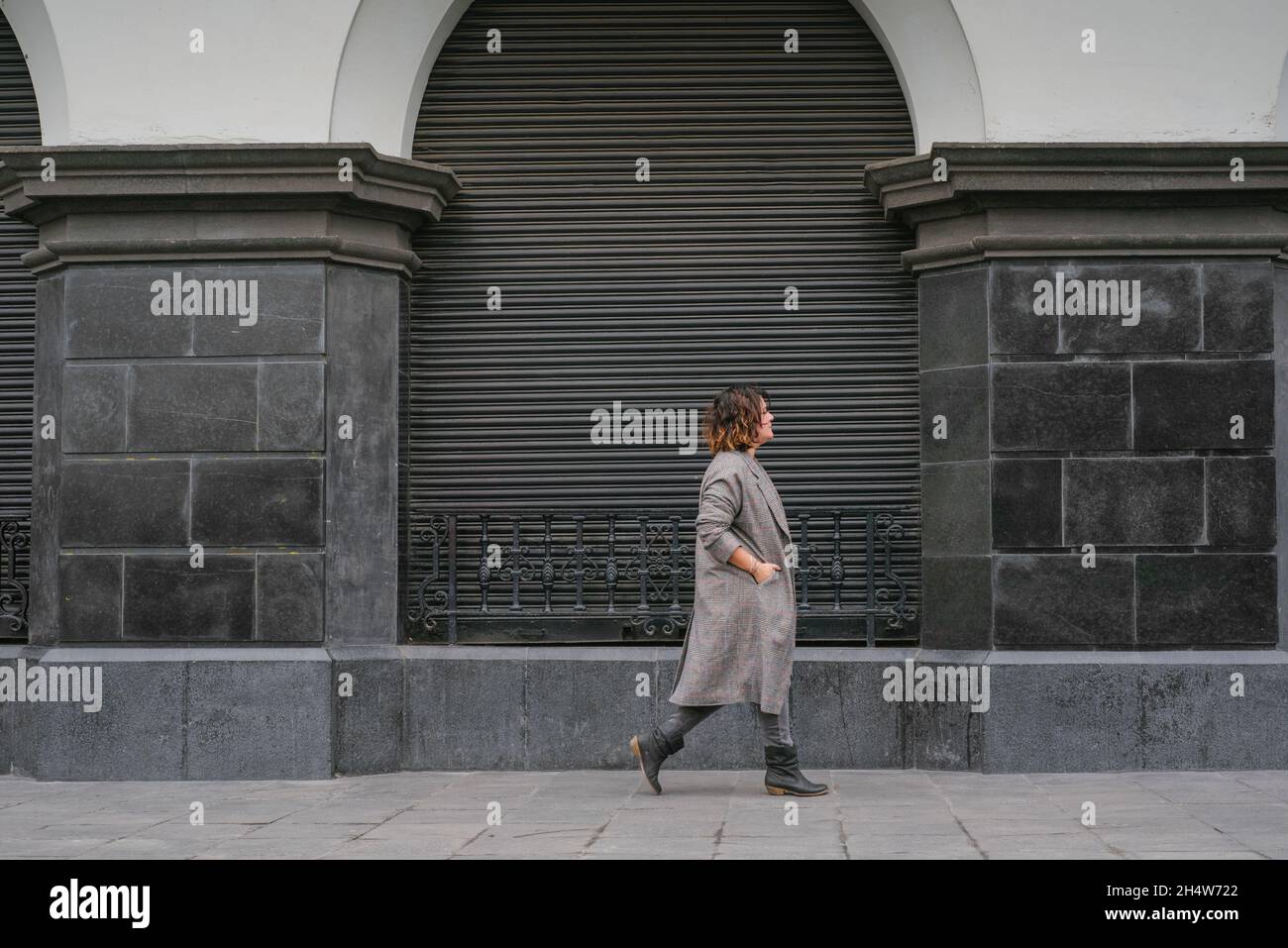 Eine Frau geht eine Straße mit antiker Architektur in der Mitte des Bildes entlang und trägt eine lange Jacke. Speicherplatz kopieren Stockfoto