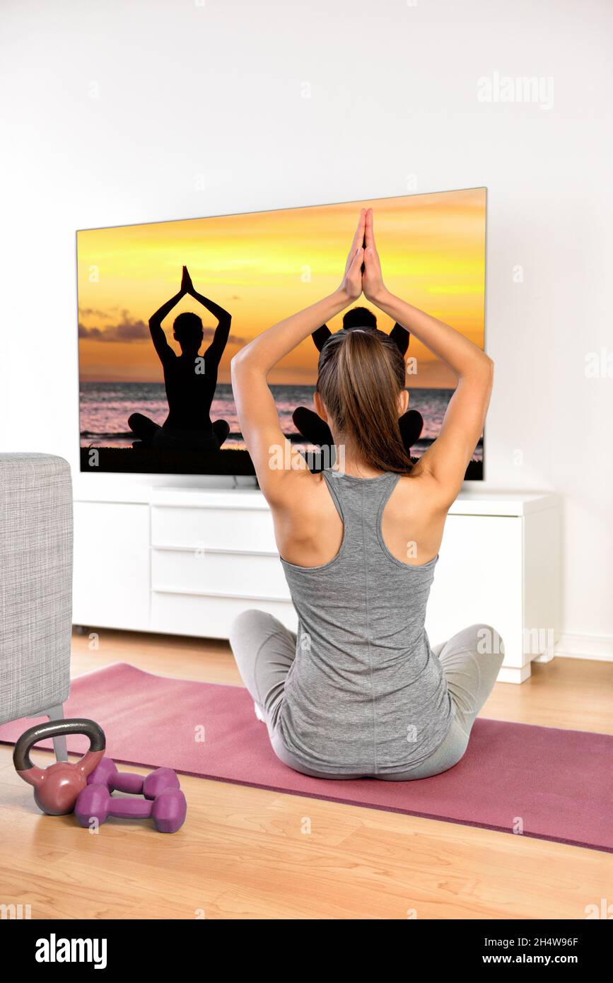 Home Workout - Frau beim Training beim Fernsehen auf dem Flachbildschirm Fitness-Programm Yoga-Training im Wohnzimmer. Yoga-Mädchen, die Meditationsübung an Stockfoto