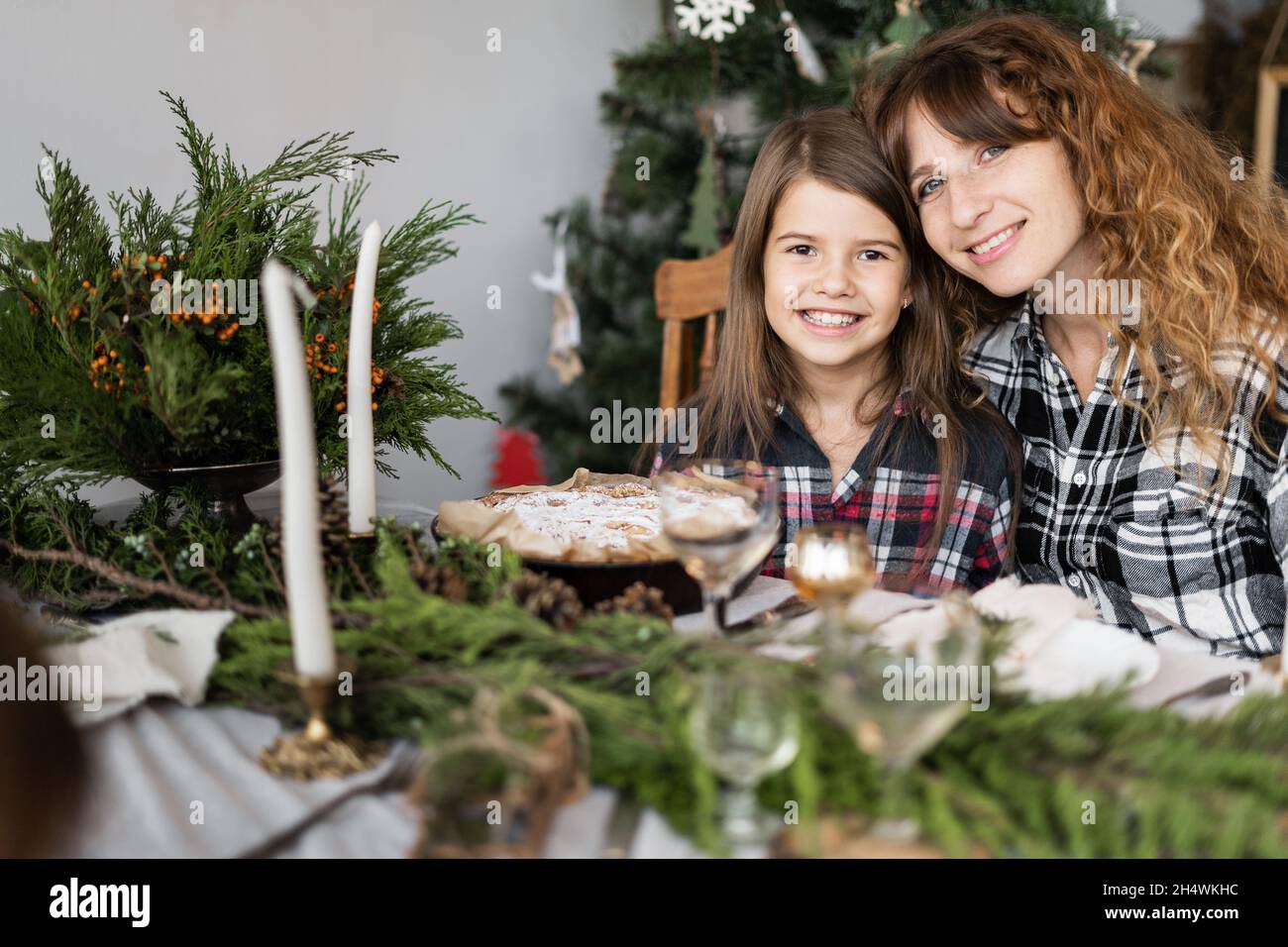 Familie zu Weihnachten am Festtisch. Portrait einer glücklichen Mutter und Tochter an einem dekorierten Tisch im Wohnzimmer. Kerzen, Zweige Stockfoto