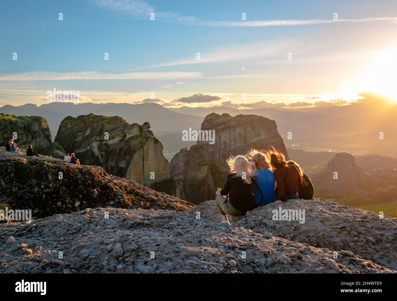 Junge Leute stehen auf dem Gipfel der Meteora und genießen den Sonnenuntergang. Stockfoto
