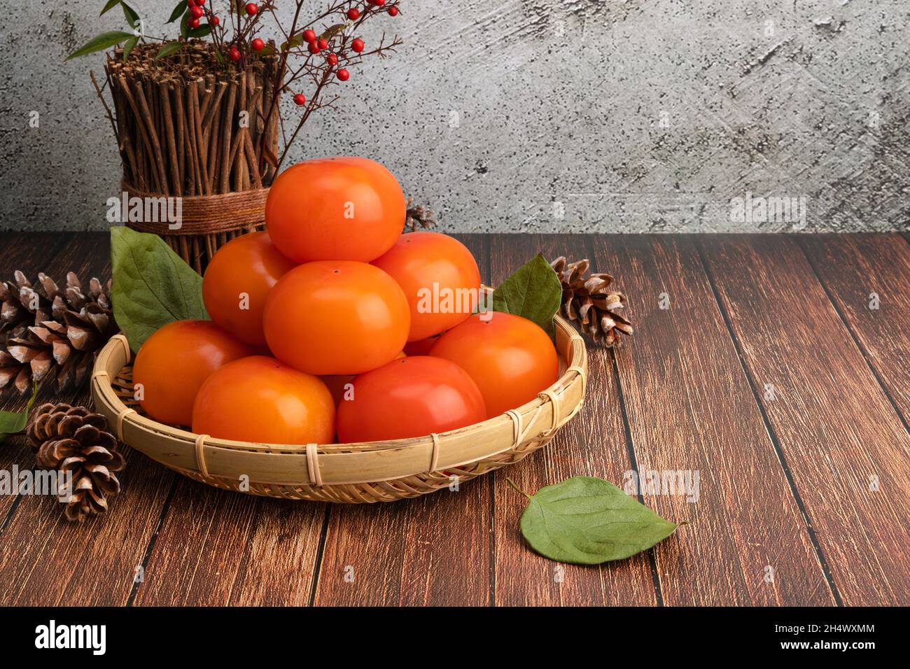 Reife Kaki in einem Bambuskorb. Holztisch Hintergrund mit einem Satz von Kaki auf der linken Seite. Stockfoto