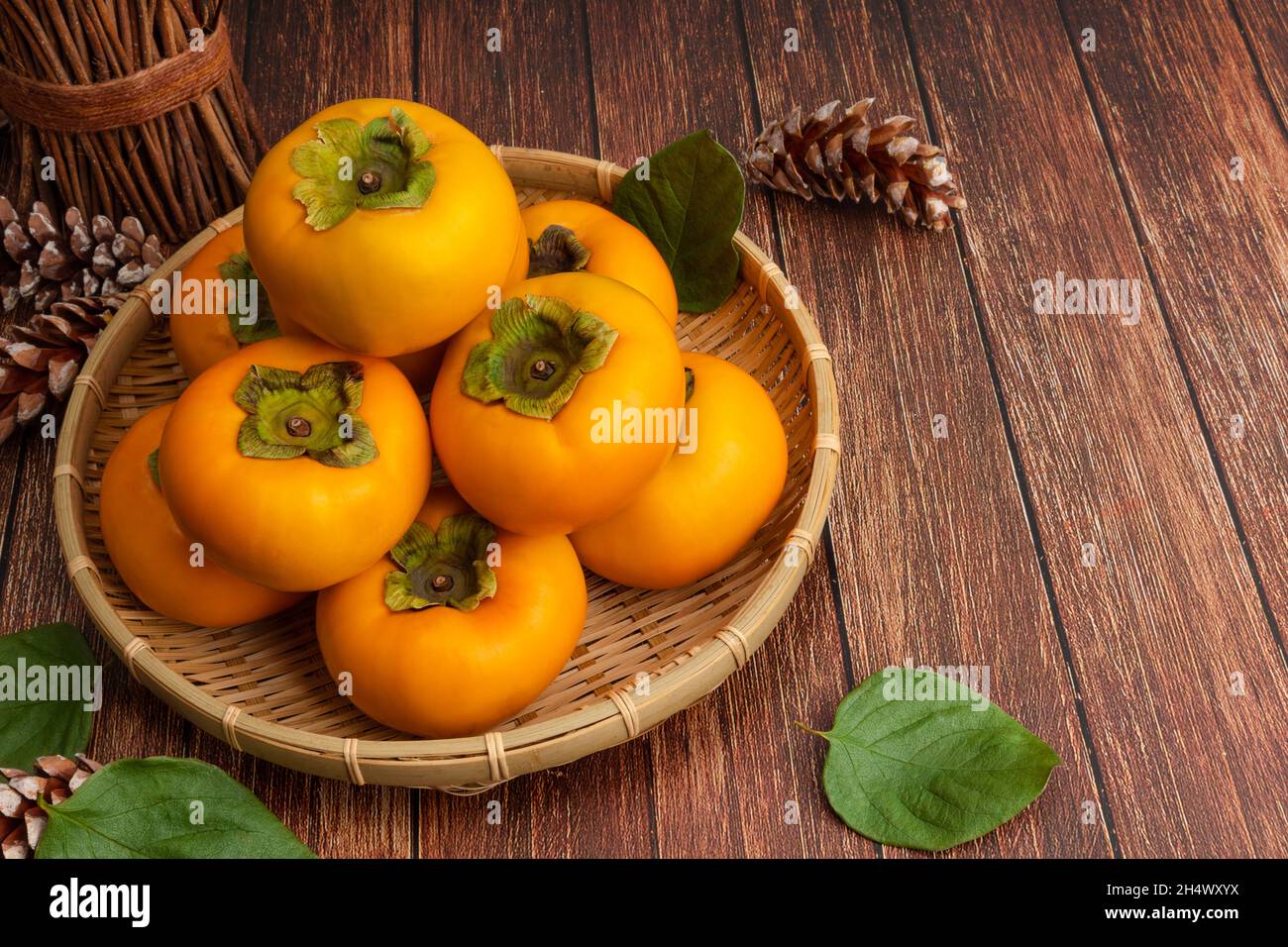 Süße Kaki im Bambuskorb. Draufsicht, Holztisch Hintergrund und Kaki Set. Stockfoto