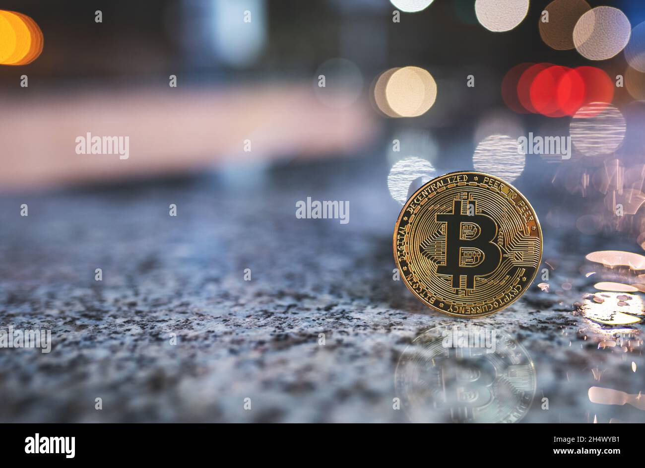 Bitcoin Krypto-Münze mit Kopieplatz, draußen stehend mit verschwommenem Bokeh Nacht Stadt Lichter Hintergrund und Reflexion auf nasser Oberfläche. Einzelnes BTC-Kryptowährungs-Token-Banner, weicher Fokus Stockfoto