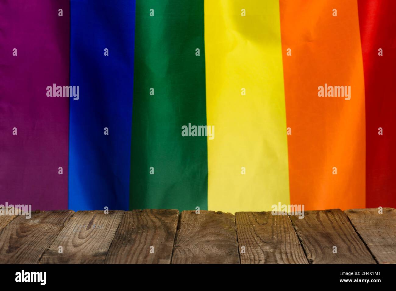 Leerer rustikaler Holztisch, mit leerem Platz für das Produkt in der Mitte, aus alten Brettern mit Stolz Regenbogenfahne auf dem Hintergrund. Stockfoto