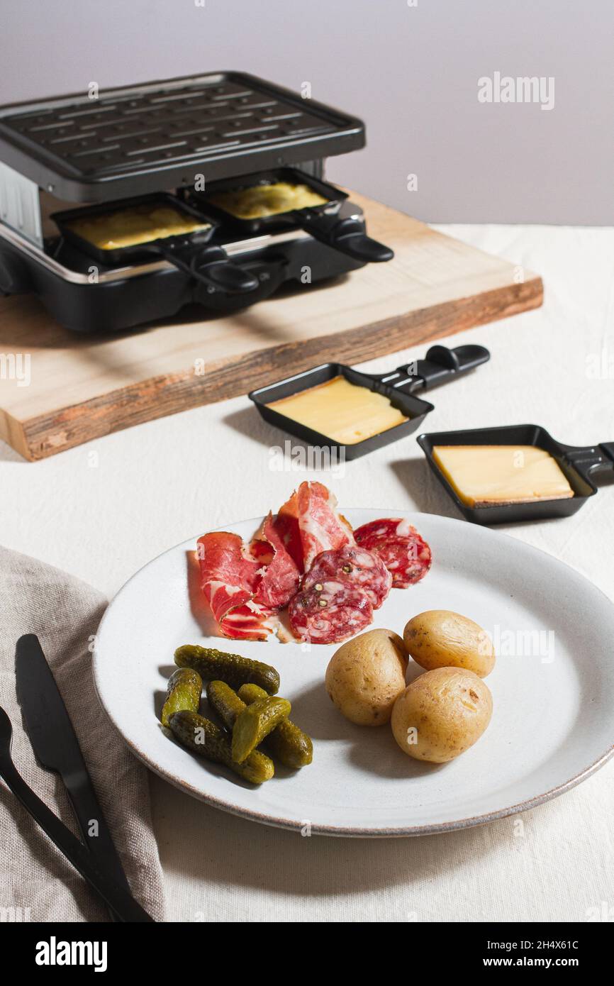 Traditionelles Raclette-Gericht mit neuen Kartoffeln, Wurstwaren und Gurken. Stockfoto
