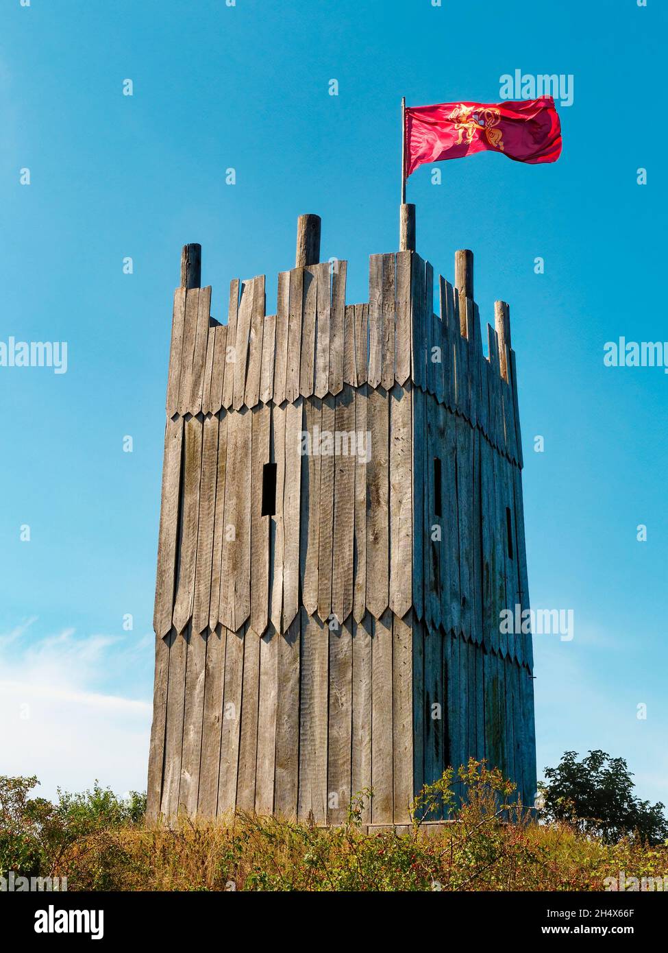 Hölzerner Turm des wikingerdorfes mit wikingerfahne, die gegen den klaren blauen Himmel schwenkt Stockfoto