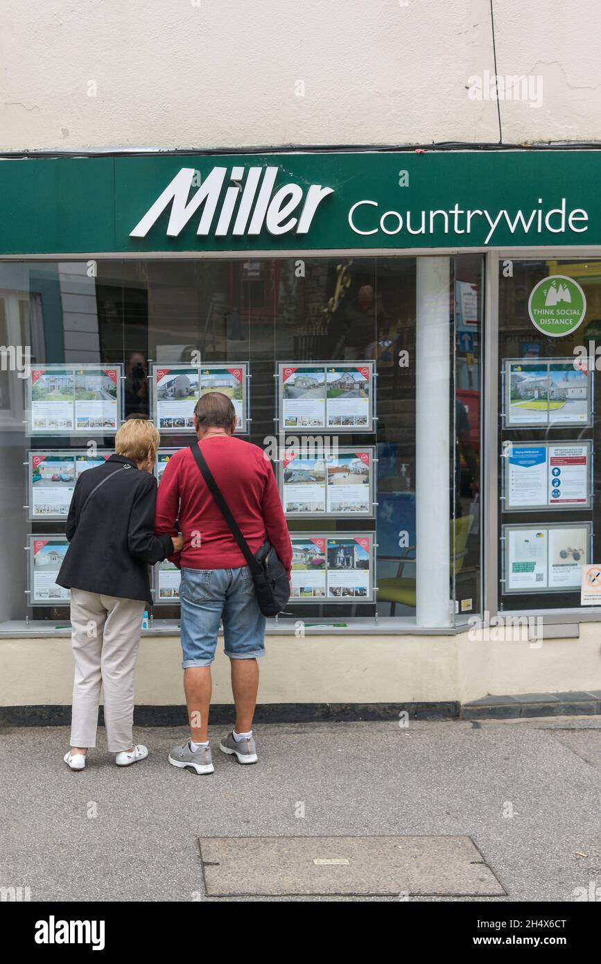 Ein reifes Paar, das sich Immobilien im Fenster eines Miller Countrywide Estate Agents in Falmouth in Cornwall ansieht. Stockfoto