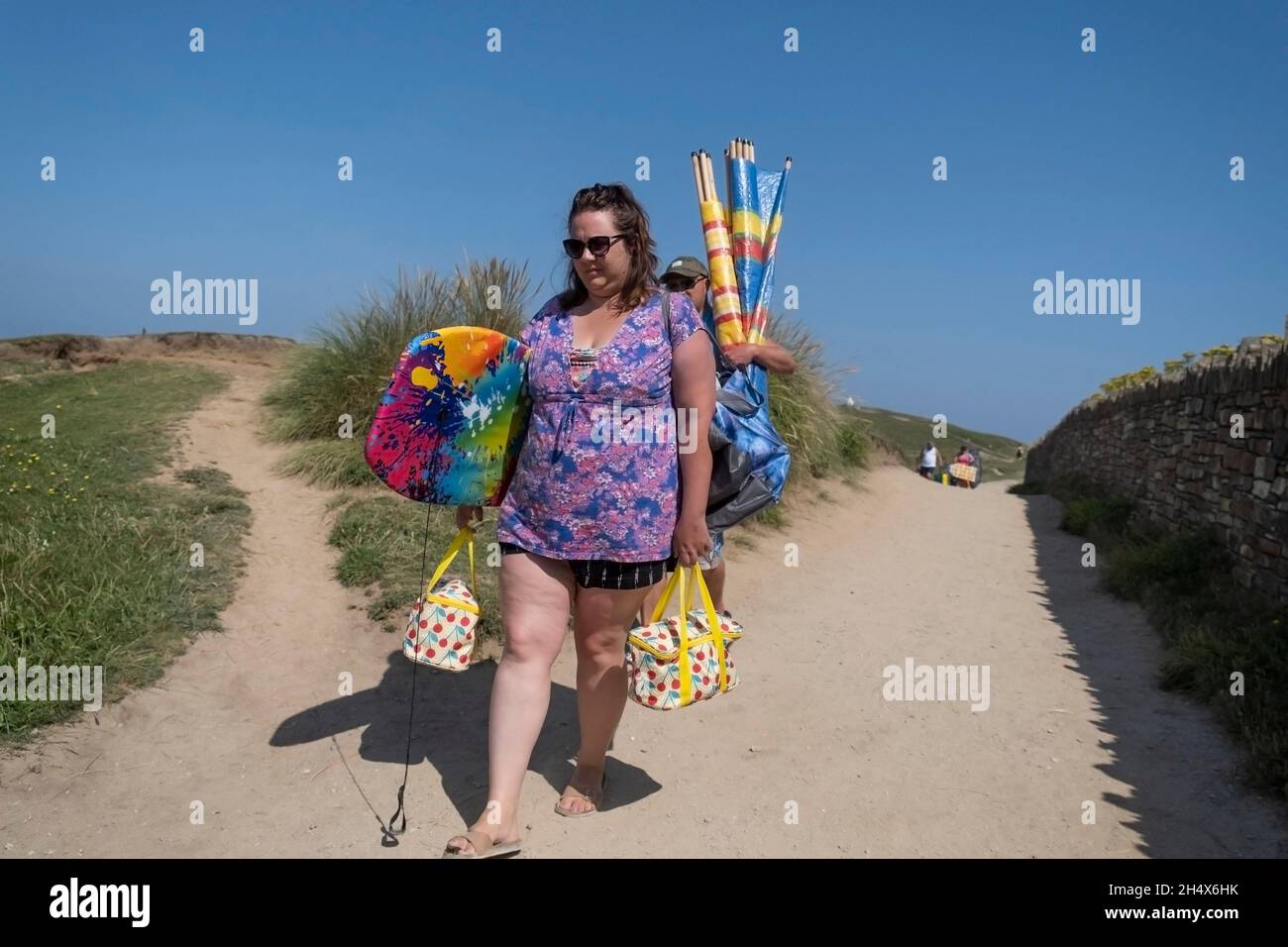 Urlauber, die in der intensiven Sommersonne von Fistral in Newquay in Cornwall mit ihren Strandunterkünften kämpfen, müssen ihre Strandhütten tragen. Stockfoto