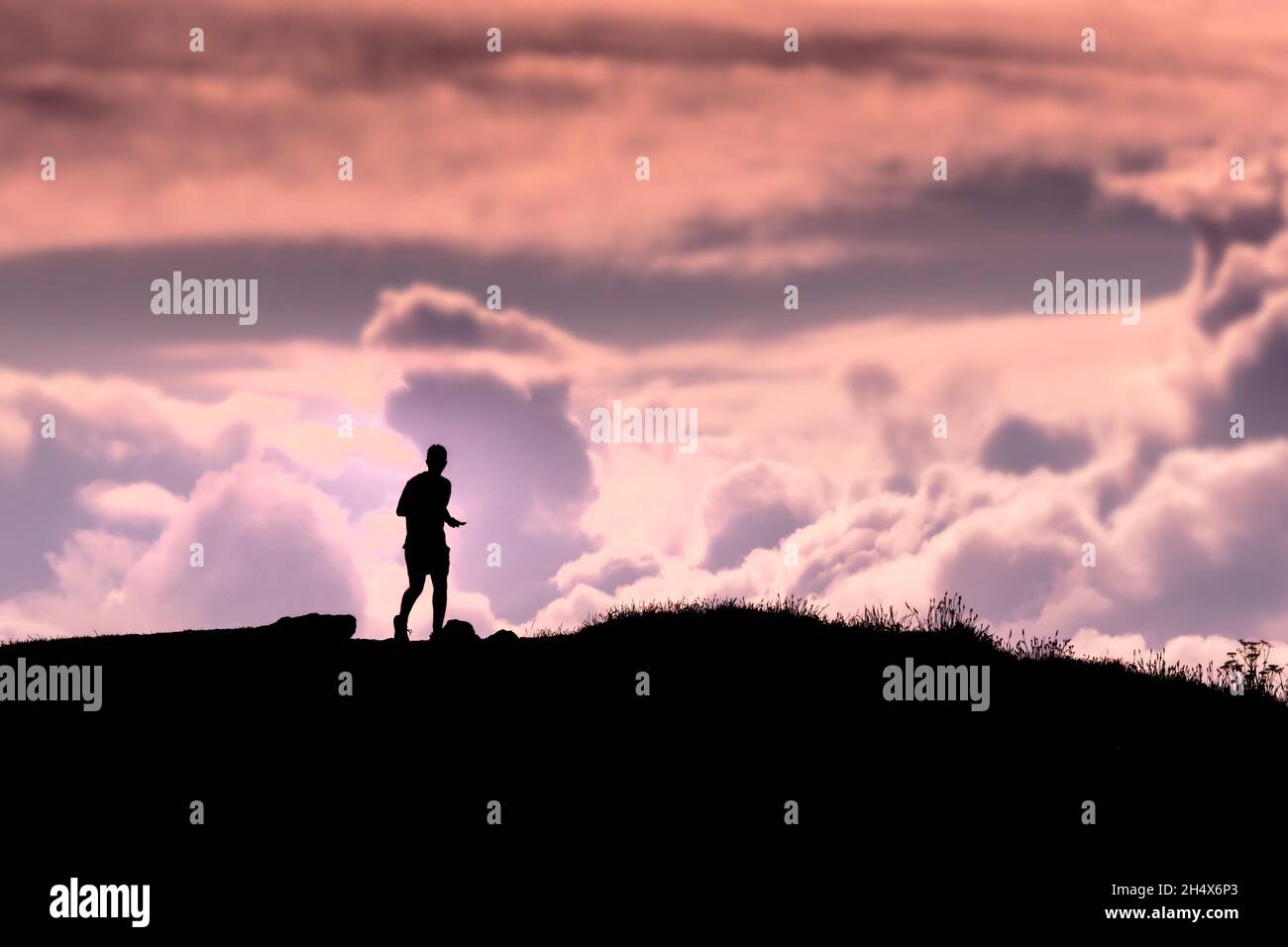 Die Silhouette eines Läufers auf dem Pentire Point East bei einem farbenfrohen Sonnenuntergang in Newquay in Cornwall. Stockfoto
