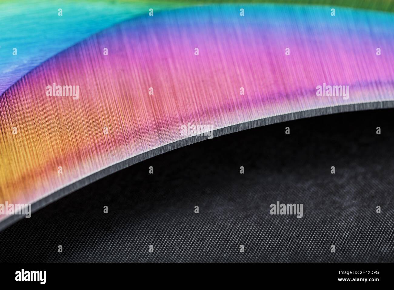 Die geschwungene, scharfe Klinge des Kerambit Dolches ist eine verlaufende Regenbogenfarbe auf einem dunklen Hintergrund. Kalter Stahl, Nahaufnahme Stockfoto