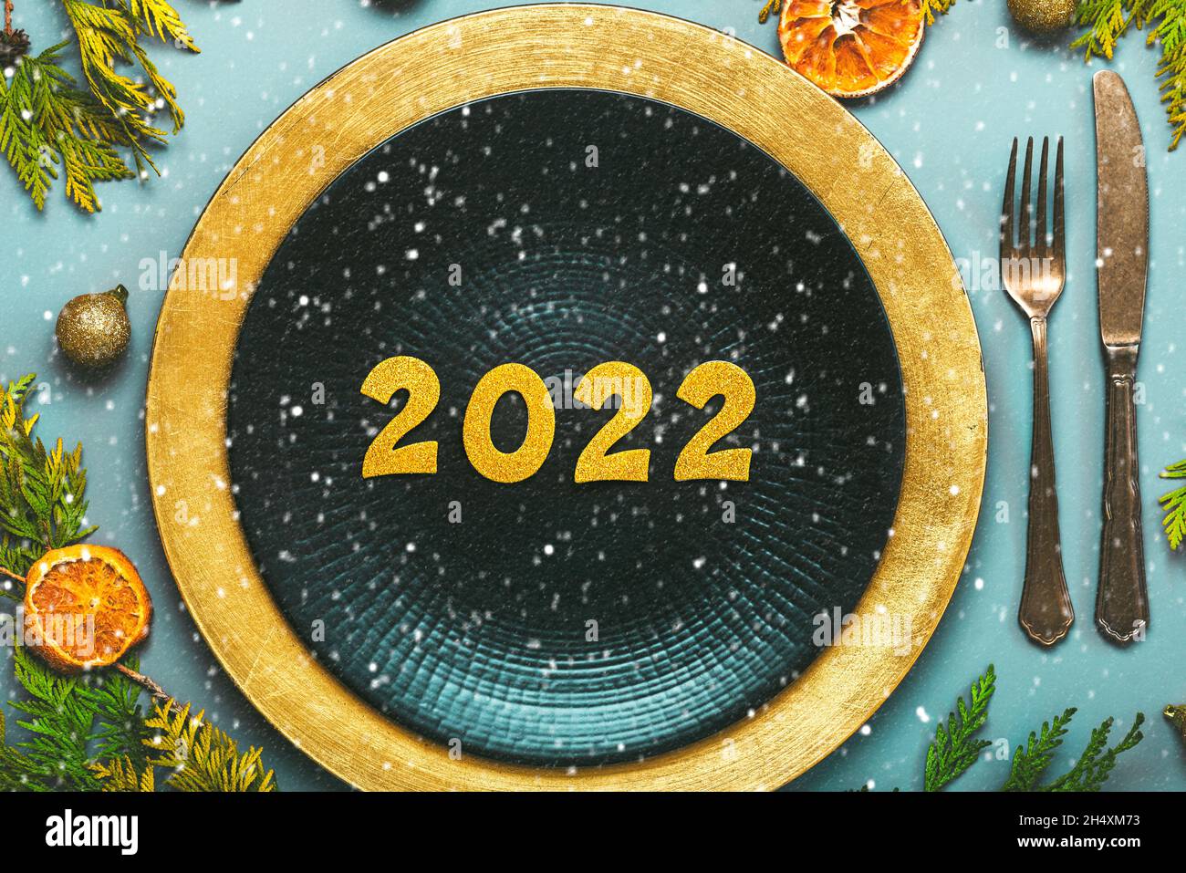 Frohes neues Jahr 2022. Draufsicht auf goldene Zahlen 2022 auf dem Teller zum Weihnachtsessen und Schneeflocken auf blauem Hintergrund. Silvesterfeier konz Stockfoto