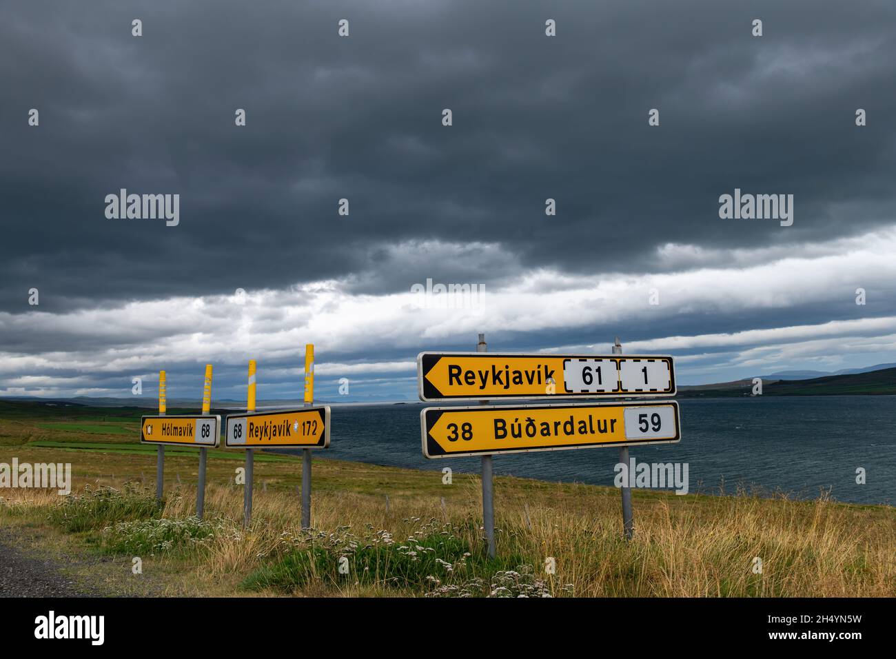 Nahaufnahme von hellgelben Straßenschildern im Nordwesten Islands entlang des Hrutafjordur (Fjord) mit typischer dunkler und heller Wolkendecke über dem Stockfoto