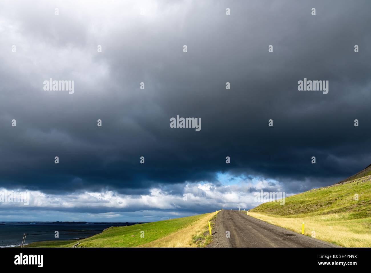 Low-Angle-Ansicht einer sonnenbeschienenen Schotterstraße und grünen Weide im nördlichen Teil Islands mit darüber großen dunklen dramatischen Regenwolken Stockfoto