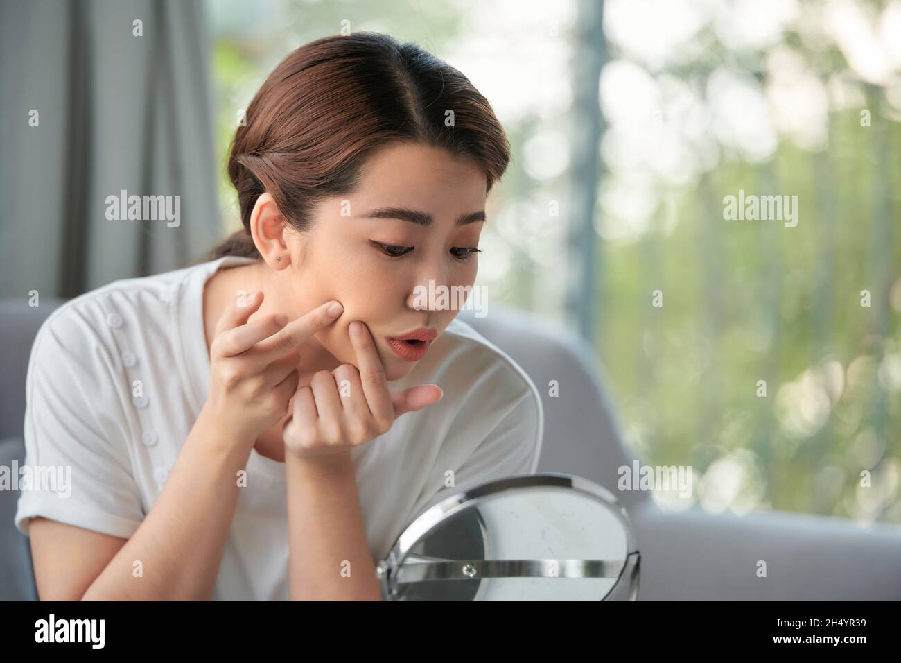 Frau untersucht ihr Gesicht im Spiegel, problematisches Akne-neigendes Hautkonzept Stockfoto