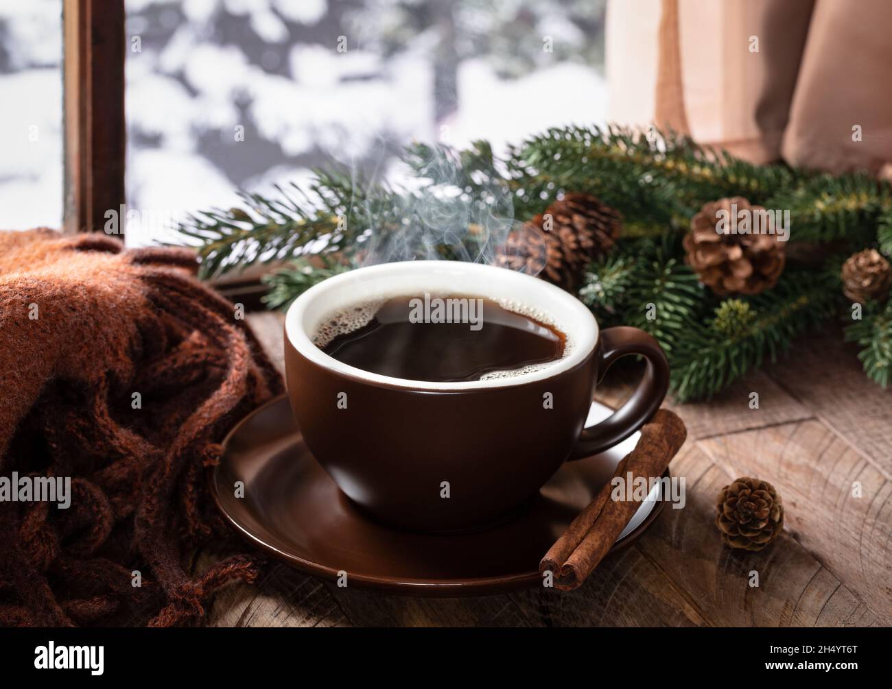 Dampfende heiße Tasse Kaffee auf einem rustikalen Holztisch an einem Fenster mit winterlichem Hintergrund im Freien Stockfoto
