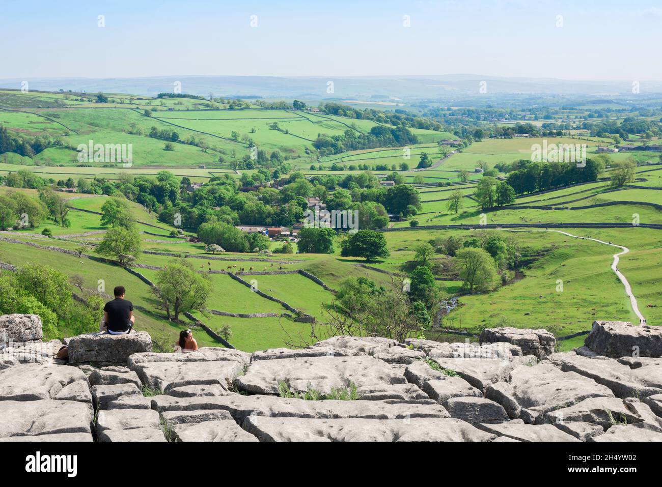 Malham Cove, Blick im Sommer auf Menschen, die in der Nähe der Klippe des Kalksteinpflasters in Malham Cove sitzen und die Yorkshire Dales, England, betrachten Stockfoto