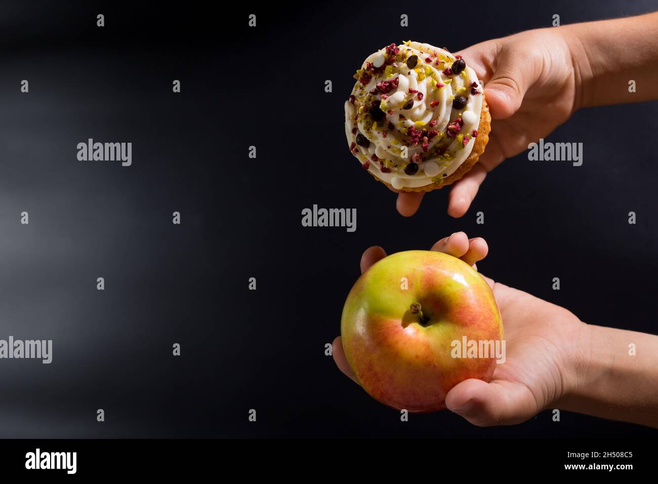 Kinderhände, die die Wahl zwischen Apfel und süßem Cupcake auf Schwarz mit Kopierfläche treffen. Stockfoto