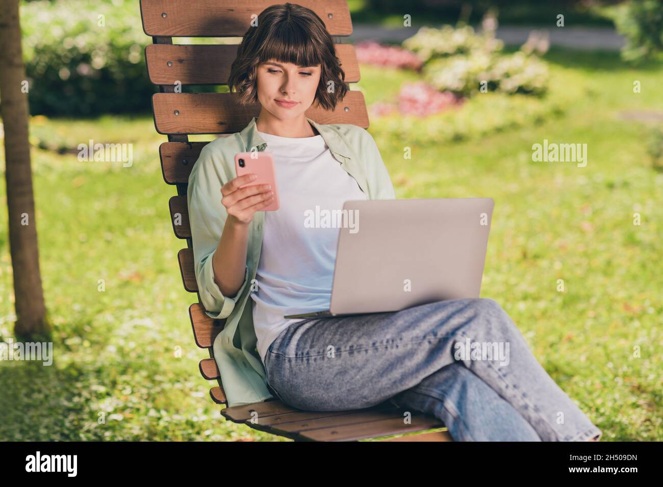 Portrait Foto lächelnd junges Mädchen auf der Bank sitzen auf Laptop mit Smartphone arbeiten Stockfoto