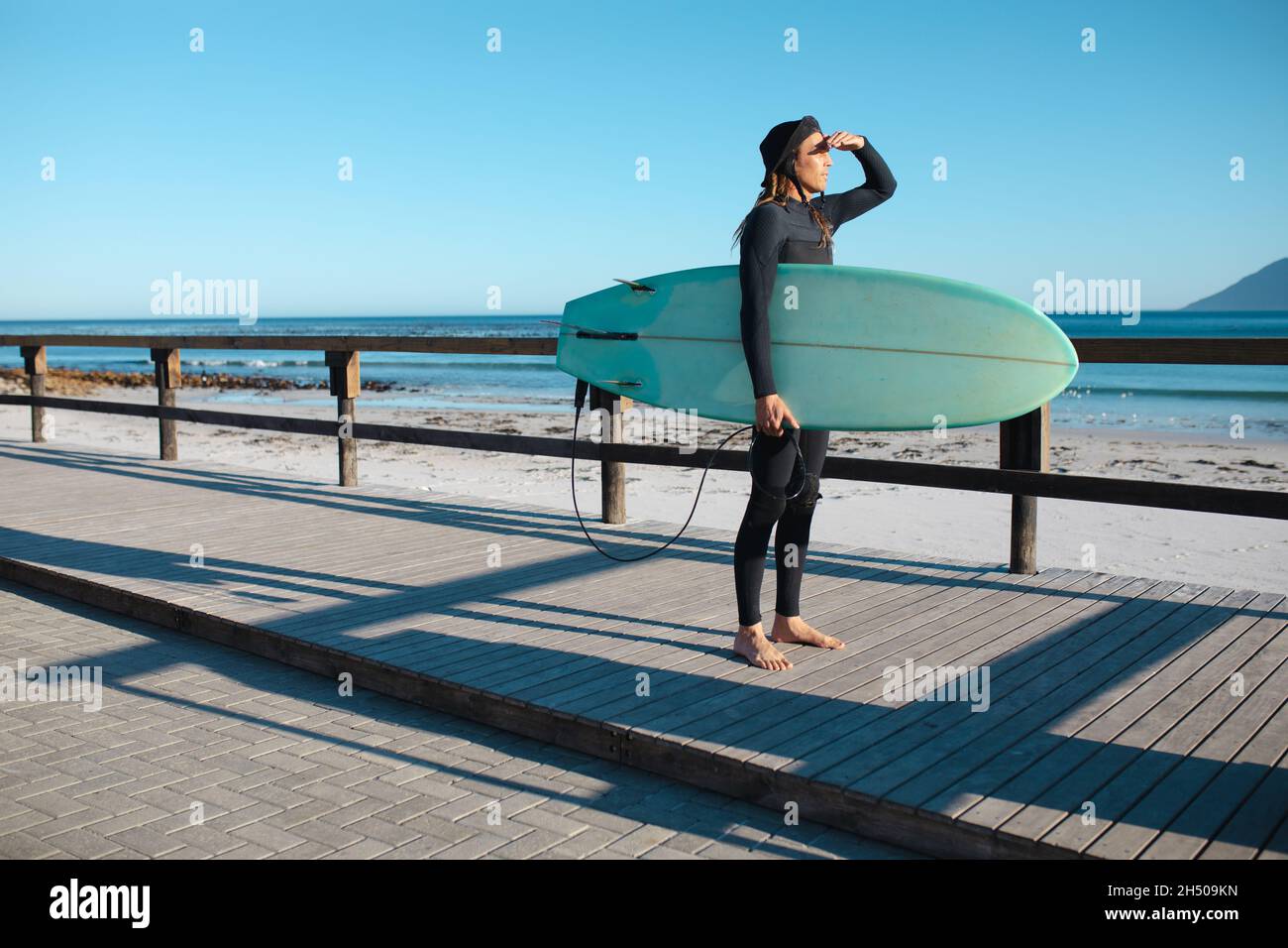 Männlicher Surfer, der am Strand auf dem Bodenbrett steht und dabei die Augen des Surfboards trägt Stockfoto